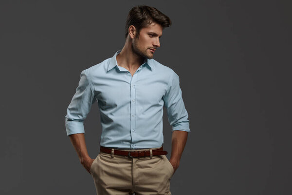 Профиль молодого вдумчивого красивого европейского бизнесмена с руками в карманах. На переднем плане бородатый мужчина с темными волосами носит официальную рубашку. Изолирован на темно-сером фоне. Студийные съемки Копирование пространства