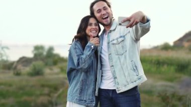 Gülümseyen adam ve kadın dışarıda telefonda selfie çekiyorlar.