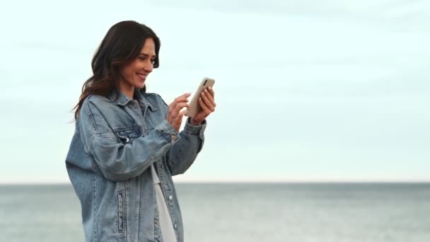 Gülümseyen Kadın Deniz Kenarında Telefonla Mesaj Atıyor — Stok video