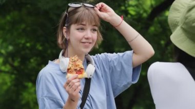 Arkadaşıyla konuşan ve elinde bir dilim pizza tutan güzel bir kadın.