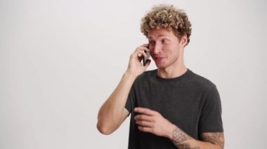 Beyaz stüdyoda telefonla konuşan kıvırcık saçlı, gülen adam.