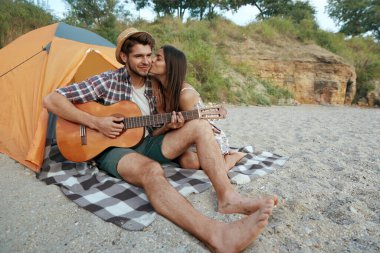 Mutlu adam onu öpen güzel bir kıza gitarla çalıyor. Genç Avrupalı çift kumsalda dinleniyor. Romantik ilişki ve birlikte vakit geçirme kavramı. Yaz tatilinde kamp yapmak