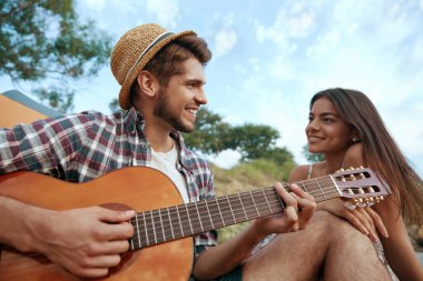 Gülümseyen adam, güzel ve mutlu bir kıza gitarla çalar. Birbirine aşık genç Avrupalı çift kumsalda dinleniyor. Romantik ilişki ve birlikte vakit geçirme kavramı. Yaz mevsiminde doğada tatil