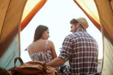 Genç Avrupalı çiftin sahilde dinlendiği çadır manzarası. Sevgilisini kucaklayan bir adam. Memnun erkek ve kız. Romantik ilişki ve birlikte vakit geçirme kavramı. Yaz tatilinde kamp yapmak