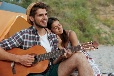 Gülümseyen adam güzel kızına gitar çalıyor. Genç Avrupalı çift kumsalda dinleniyor. Romantik ilişki ve birlikte vakit geçirme kavramı. Doğada kamp yapmak. Yaz zamanı.