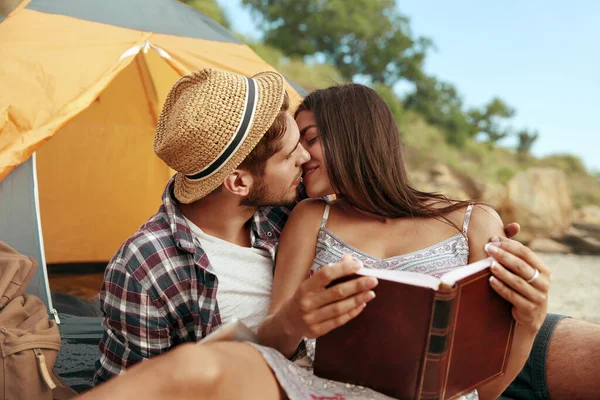欧洲的一对年轻夫妇在海滩上相亲相爱 高兴的女孩拿着书 浪漫关系的概念和享受在一起的时光 夏天在大自然的露营度假 — 图库照片