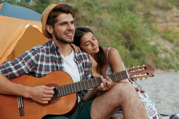 Gülümseyen adam güzel kızına gitar çalıyor. Genç Avrupalı çift kumsalda dinleniyor. Romantik ilişki ve birlikte vakit geçirme kavramı. Doğada kamp yapmak. Yaz zamanı.