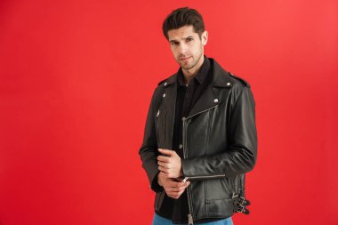 Deri ceketli genç adam kırmızı duvardan izole edilmiş kameraya bakıyor.