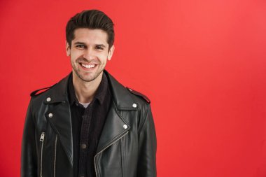 Deri ceketli genç adam kırmızı duvardan izole edilmiş kameraya gülümsüyor.