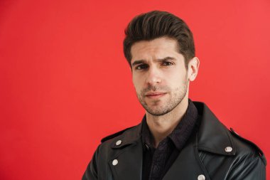 Deri ceketli genç adam kırmızı duvardan izole edilmiş kameraya bakıyor.