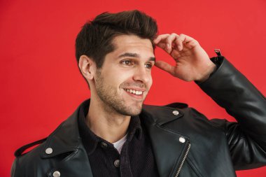 Tıraşsız, deri ceketli genç adam kırmızı duvarın üstünde sırıtıyor.