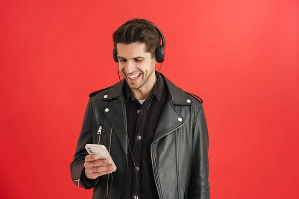 Kırmızı Duvardan Izole Edilmiş Cep Telefonu Kulaklık Kullanarak Gülümseyen Genç — Stok fotoğraf