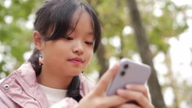 Düşünceli Asyalı küçük kızın parkta telefonla yazışının alt görüntüsü