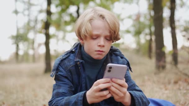 一个多愁善感的小男孩在森林里用电话打字 — 图库视频影像