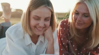 Piknikte ekose üzerinde uzanmış telefona bakan mutlu kadınların yakın plan görüntüsü.