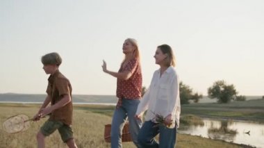 Yakışıklı aile konuşuyor ve nehir kenarında piknikte yürüyor.