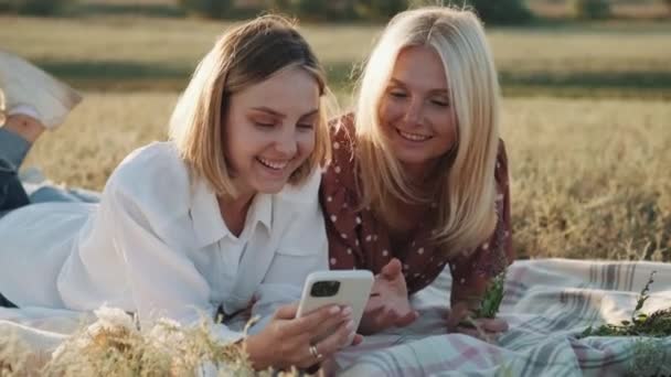 Két Mosolygó Nézi Telefont Miközben Kockás Pikniken Fekszenek — Stock videók