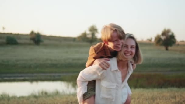 Sorridente Mamma Porta Suo Figlio Sulla Schiena Vicino Fiume — Video Stock