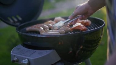 Erkek ellerinin açık havada ızgara sosis çevirdiği yakın çekim görüntüsü.