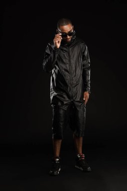 Siyah arka planda izole edilmiş güneş gözlüklü genç adam kameraya poz veriyor.