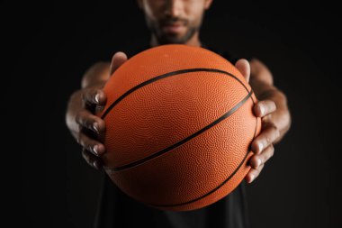 Genç sporcu siyah arka planda izole edilmiş kameraya bakıyor ve basketbola uzanıyor