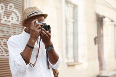 Siyahi adam Avrupa 'da dijital kamerada fotoğraf çekiyor. Genç adam hasır şapka, beyaz gömlek ve kol saati takıyor. Turizm ve seyahat kavramı. Serbest çalışmanın bir fikri. Güneşli gündüz