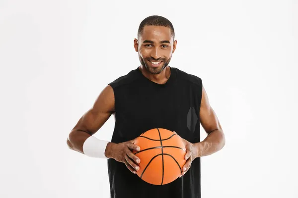 年轻的黑人运动员一边在镜头前微笑 一边与被白色背景隔开的篮球合影 — 图库照片
