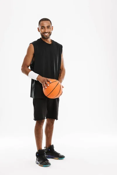 年轻的黑人运动员一边在镜头前微笑 一边与被白色背景隔开的篮球合影 — 图库照片