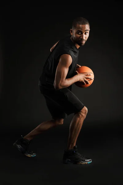 年轻的毛茸茸的运动员一边打篮球 一边在黑暗的背景下打篮球 — 图库照片