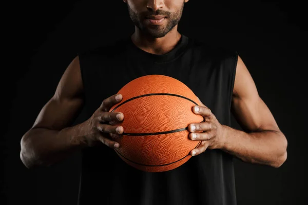 年轻的运动员一边拿着黑色背景的篮球 一边看着镜头 — 图库照片