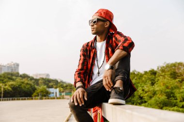 Sıradan giyinmiş genç Afrikalı bir adam korkuluklarda oturuyor.