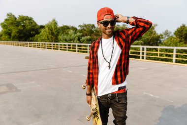 Genç siyah adam dışarıda kaykay yaparken gülümsüyor.