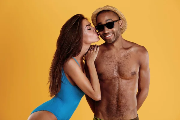 女孩吻着她微笑的男朋友 年轻漂亮的浪漫夫妇 黑人男子和欧洲女子穿着海滩服装 暑期海滩度假的概念 被黄色背景隔离 工作室拍摄 — 图库照片