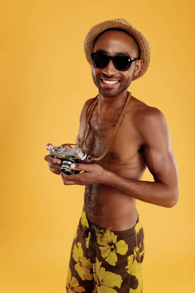 若い笑顔ハンサムな黒人男性古いカメラを保持します 男は水泳パンツ わら帽子と眼鏡を着用してください 夏のビーチ休暇の概念 黄色の背景に隔離された スタジオ撮影 — ストック写真