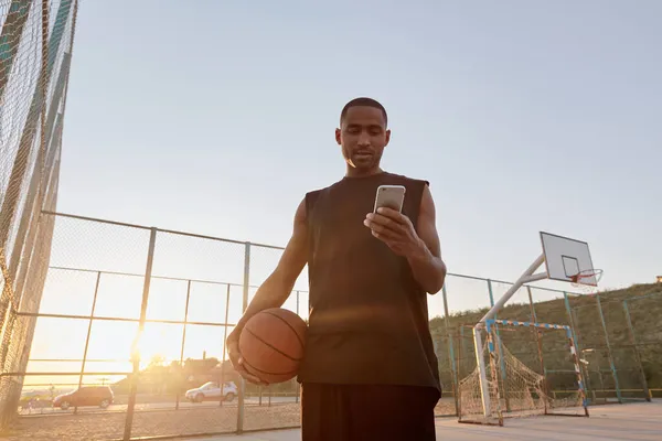 Pemuda Afrika Yang Berkonsentrasi Memegang Bola Basket Dan Menggunakan Ponsel — Stok Foto