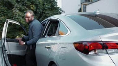 Gülümseyen baba arabada oğluna kapıyı açıyor ve bagajı açıyor.