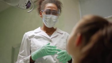 Yakışıklı Afrikalı dişçi hastasına bir şey anlatıyor ve işaret ediyor.