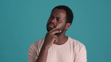 Tişört giyen dalgın Afrikalı adam mavi stüdyoda olumlu cevap veriyor.