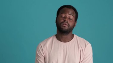 Tişört giyen sıkkın Afrikalı adam mavi stüdyoda el hareketi yapıyor.