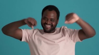 Gülümseyen Afrikalı adam tişört giyip dans ediyor ve mavi stüdyoda bana jest yapıyor.