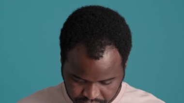 Mavi stüdyoda tişört giyen gülümseyen Afrikalı adamın yakın çekim görüntüsü.