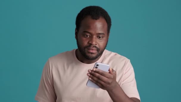 Pozitivní Překvapení Afričan Nosí Tričko Při Pohledu Telefon Modrém Studiu — Stock video