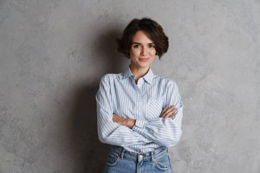 Gri duvarın üzerinden izole edilmiş, gülümseyen ve kameraya bakan genç esmer kadın.