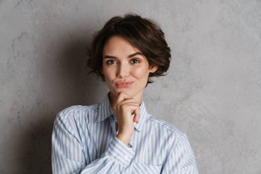 Gri duvarın üzerinden izole edilmiş, gülümseyen ve kameraya bakan genç esmer kadın.