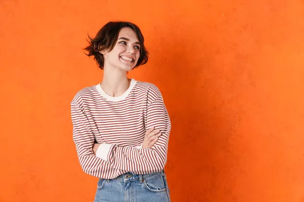 Jonge Brunette Vrouw Gestreepte Sweater Glimlachen Kijken Opzij Geïsoleerd Oranje — Stockfoto