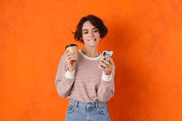 Νεαρή Μελαχρινή Γυναίκα Πίνει Καφέ Ενώ Χρησιμοποιεί Κινητό Τηλέφωνο Απομονώνονται — Φωτογραφία Αρχείου