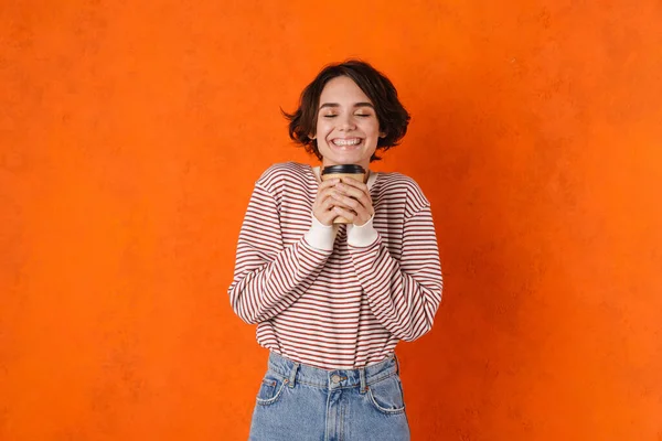 若いですブルネット女性笑顔ながらコーヒーを飲みながら隔離上のオレンジ壁 — ストック写真