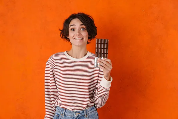 Молодая Брюнетка Улыбается Позируя Шоколадом Изолированы Над Оранжевой Стеной — стоковое фото