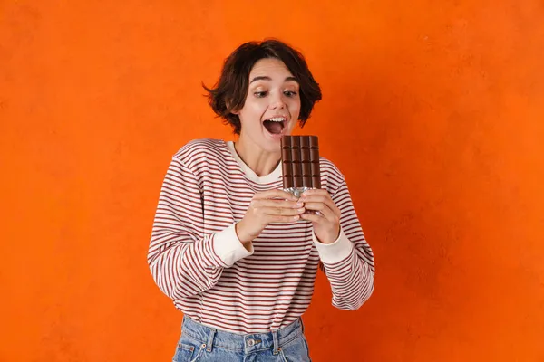 Jovem Morena Sorrindo Enquanto Come Chocolate Isolado Parede Laranja — Fotografia de Stock