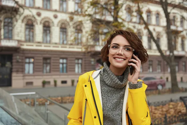 Chica Joven Impermeable Amarillo Llamando Teléfono Inteligente Mientras Camina Ciudad —  Fotos de Stock